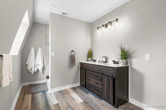 bathroom featuring double vanity, visible vents, a sink, wood finished floors, and baseboards