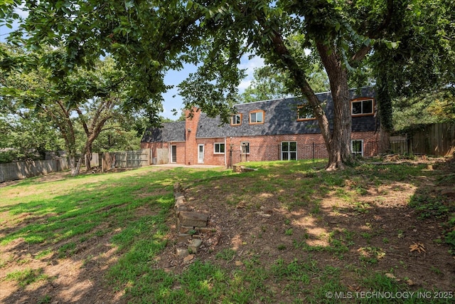 2936 Ridge Rd, Bartlesville, OK 74006 - rear view of property featuring brick siding, a fenced backyard, roof with shingles, and mansard roof