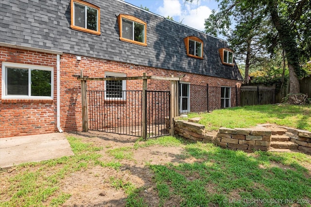 rear view of property with brick siding, fence, mansard roof, and roof with shingles