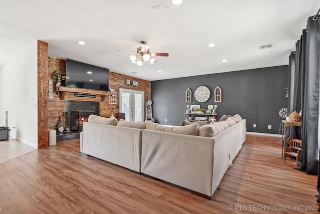 living room featuring a large fireplace, light hardwood / wood-style floors, french doors, and ceiling fan