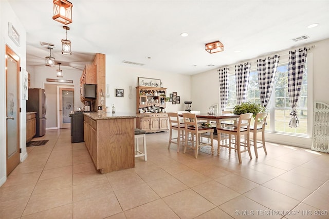 kitchen with hanging light fixtures, light stone countertops, light tile patterned floors, and stainless steel fridge