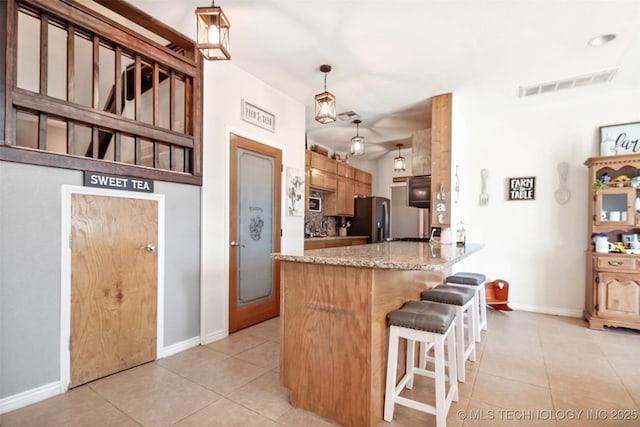 kitchen featuring light tile patterned floors, stainless steel refrigerator, hanging light fixtures, light stone countertops, and kitchen peninsula