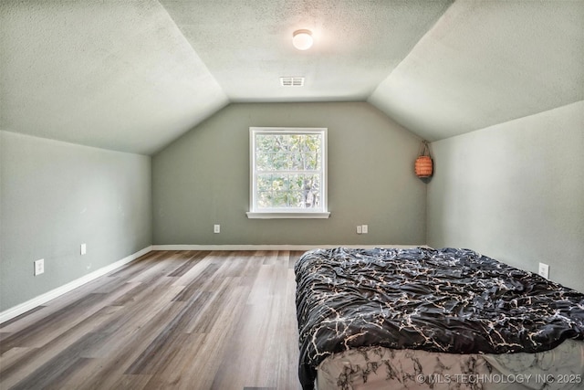 bedroom featuring hardwood / wood-style flooring, vaulted ceiling, and a textured ceiling