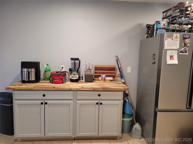 kitchen featuring light tile patterned flooring, stainless steel fridge, and butcher block counters