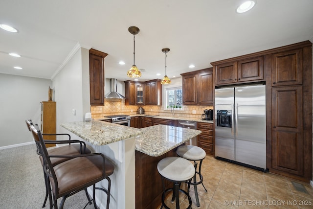 kitchen featuring a breakfast bar, hanging light fixtures, stainless steel appliances, kitchen peninsula, and wall chimney exhaust hood