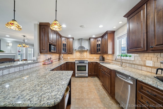 kitchen featuring wall chimney range hood, hanging light fixtures, sink, and appliances with stainless steel finishes