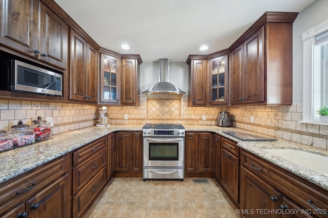 kitchen with light stone counters, appliances with stainless steel finishes, wall chimney exhaust hood, and tasteful backsplash