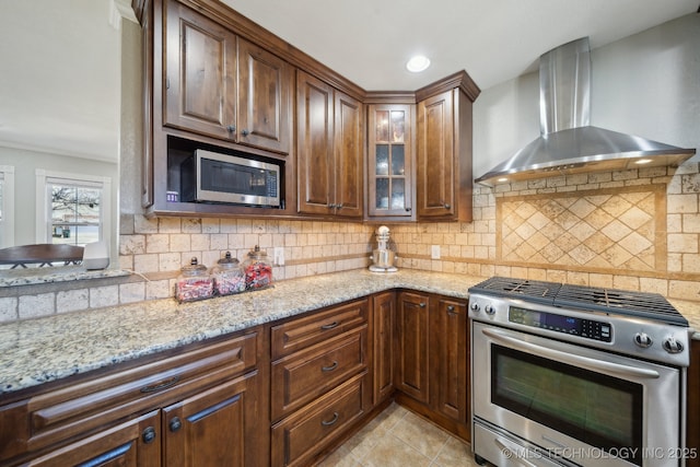 kitchen featuring stainless steel appliances, decorative backsplash, light stone counters, and wall chimney exhaust hood