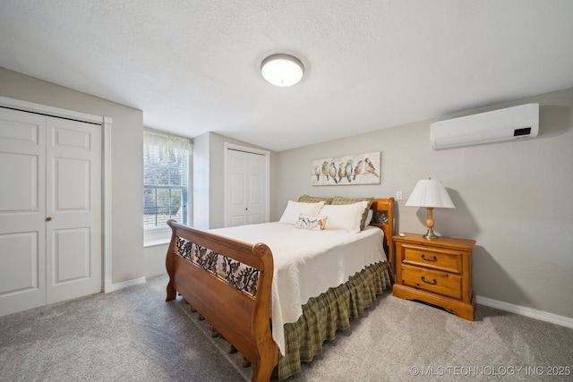 bedroom featuring multiple closets, light colored carpet, a wall mounted air conditioner, and a textured ceiling