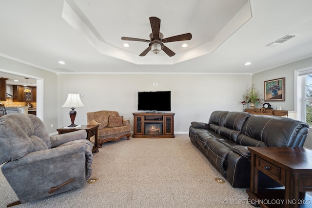 living room featuring light carpet, a tray ceiling, ornamental molding, and ceiling fan