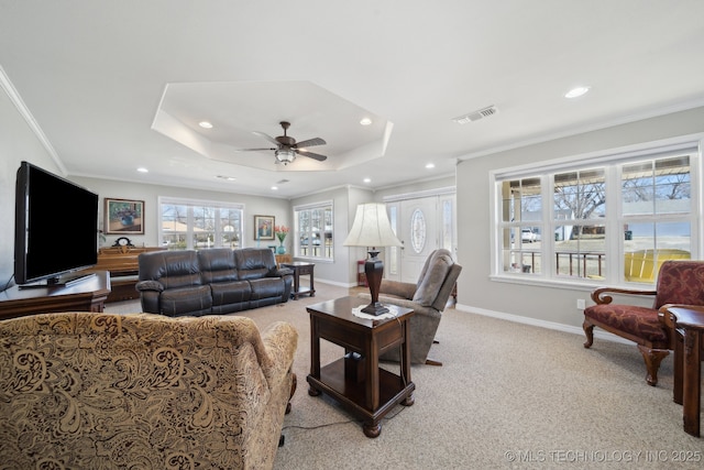 carpeted living room with a tray ceiling, ornamental molding, and ceiling fan