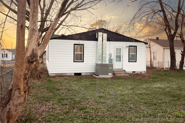 back house at dusk with a lawn and central air condition unit