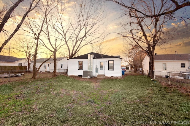 back house at dusk featuring cooling unit and a lawn