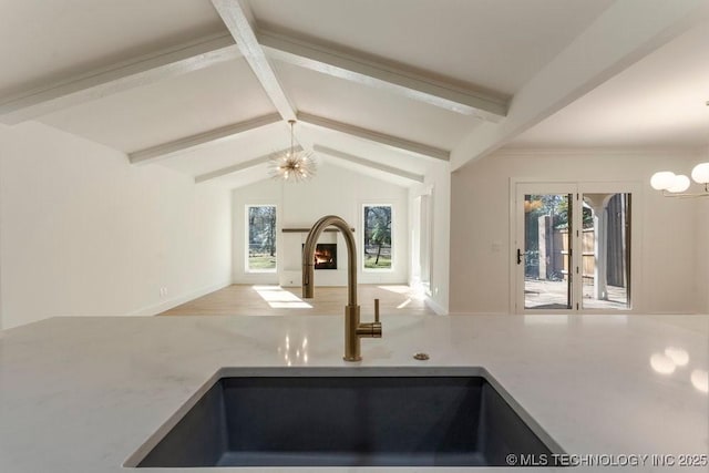 kitchen featuring a healthy amount of sunlight, sink, lofted ceiling with beams, and a chandelier