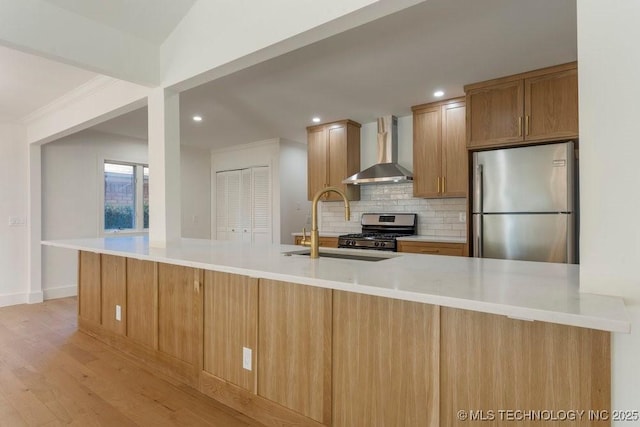 kitchen with appliances with stainless steel finishes, decorative backsplash, kitchen peninsula, light wood-type flooring, and wall chimney exhaust hood