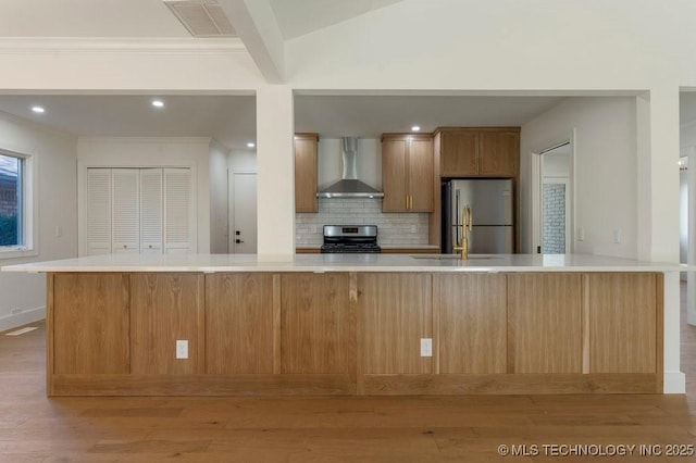 kitchen with wall chimney exhaust hood, sink, a large island with sink, appliances with stainless steel finishes, and backsplash