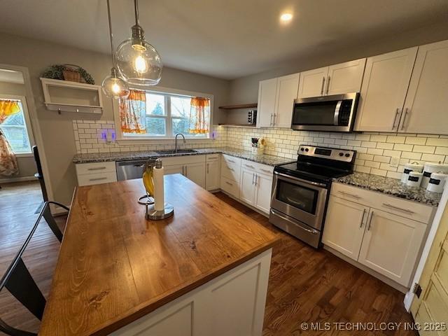 kitchen featuring dark stone countertops, decorative light fixtures, white cabinets, and appliances with stainless steel finishes