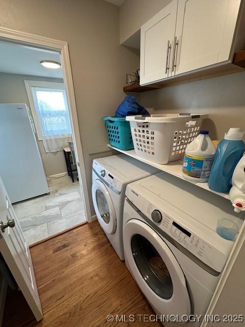 clothes washing area with cabinets, wood-type flooring, and separate washer and dryer