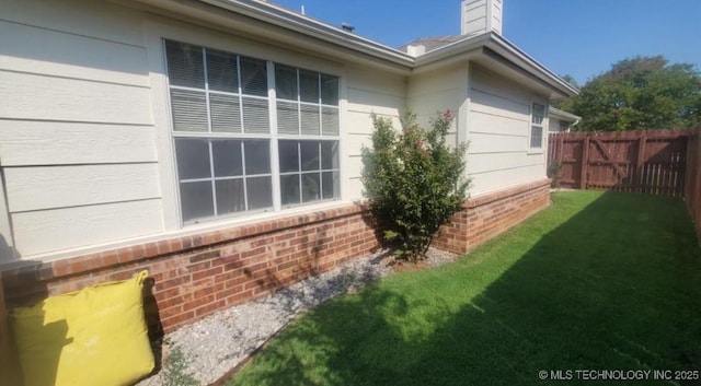 view of side of property featuring brick siding, a lawn, and fence