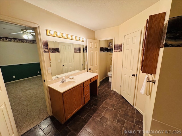 bathroom with baseboards, a ceiling fan, toilet, stone finish flooring, and vanity