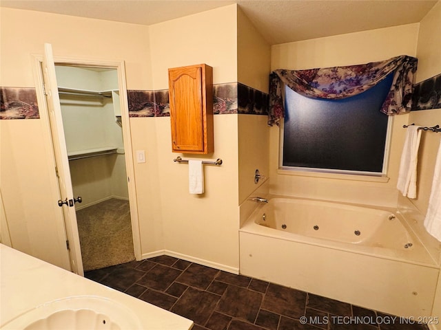 bathroom featuring a spacious closet, a tub with jets, a sink, and baseboards