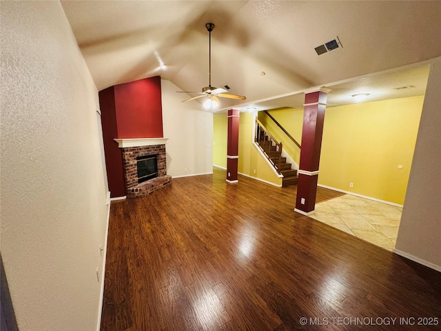 unfurnished living room featuring visible vents, stairway, wood finished floors, vaulted ceiling, and a brick fireplace