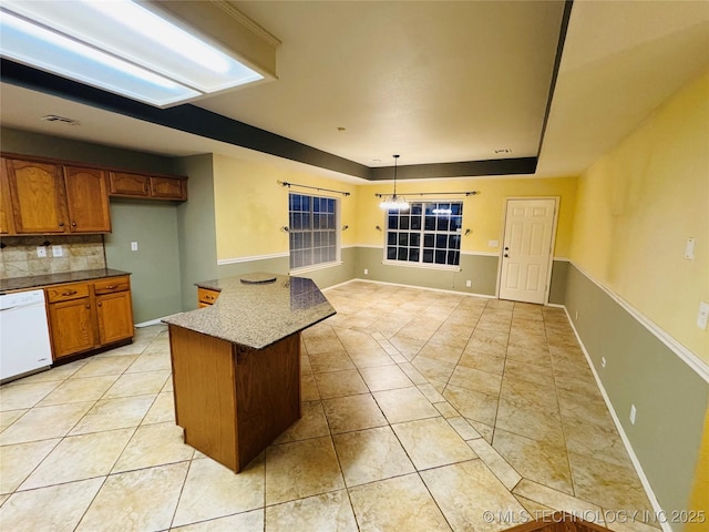 kitchen featuring light tile patterned floors, visible vents, brown cabinetry, white dishwasher, and a tray ceiling