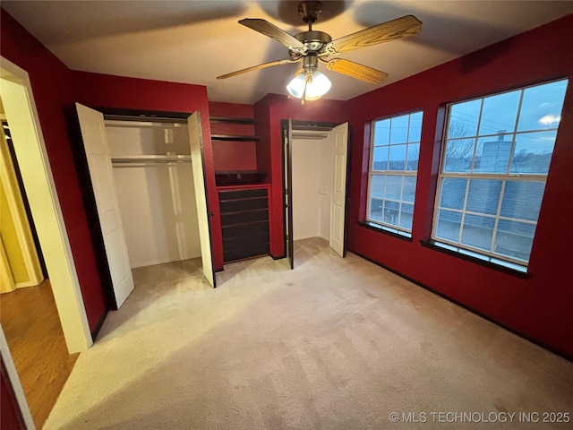 unfurnished bedroom featuring two closets, a ceiling fan, and light colored carpet