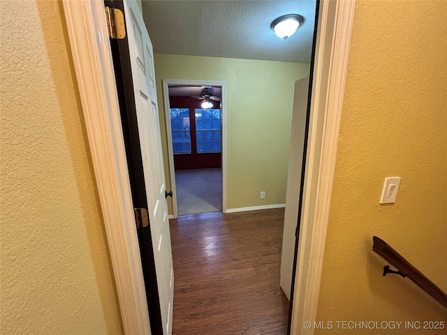 corridor featuring a textured wall, a textured ceiling, baseboards, and wood finished floors