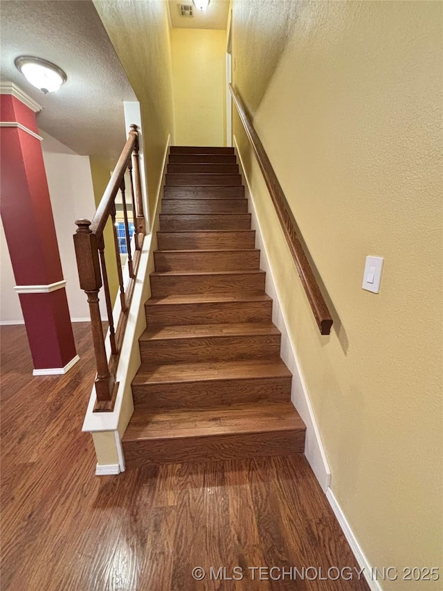 staircase featuring a textured ceiling, baseboards, and wood finished floors