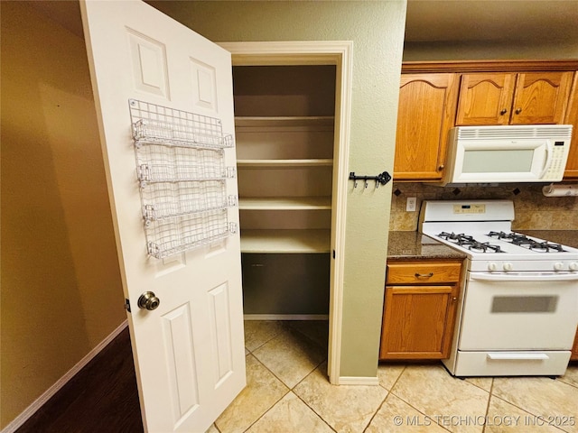 kitchen featuring white appliances, baseboards, brown cabinets, and light tile patterned flooring