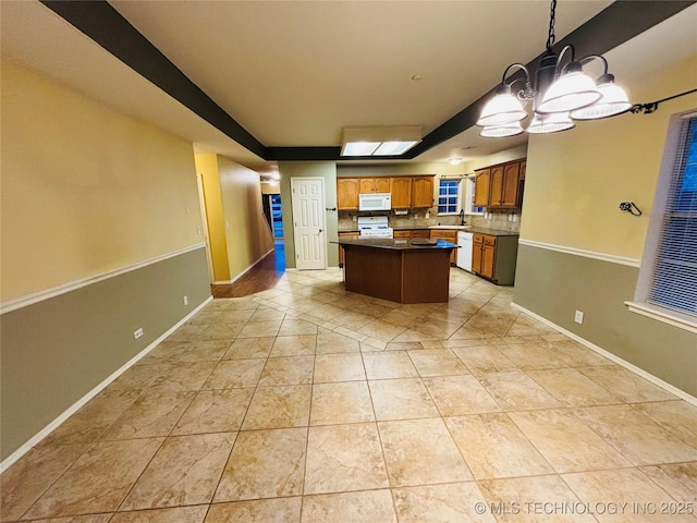 kitchen with light tile patterned floors, white appliances, a sink, baseboards, and a center island