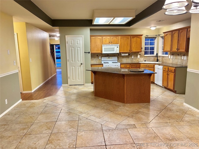 kitchen with brown cabinets, decorative backsplash, a sink, a kitchen island, and white appliances