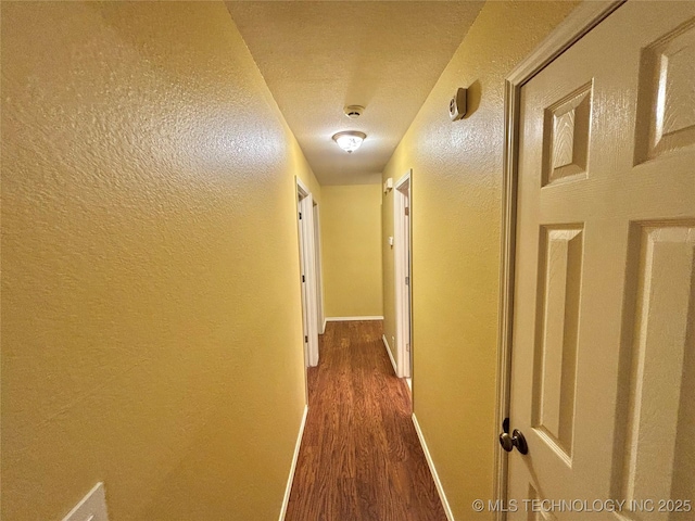 hallway with a textured wall, baseboards, and wood finished floors