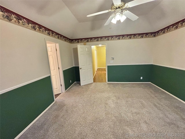 carpeted empty room featuring a ceiling fan, vaulted ceiling, and baseboards