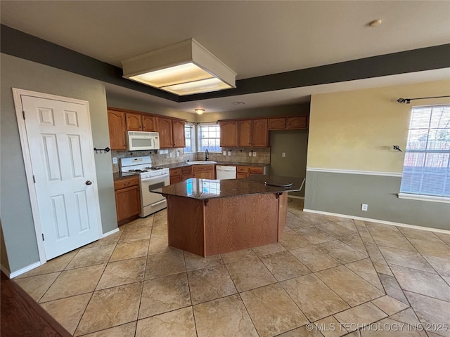 kitchen featuring a center island, decorative backsplash, brown cabinetry, a sink, and white appliances