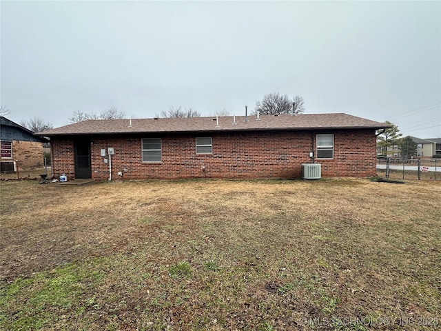 rear view of house featuring central AC unit and a lawn