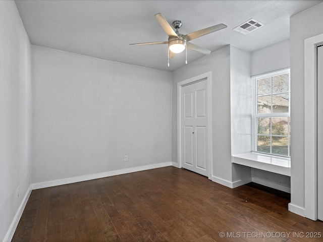 unfurnished bedroom featuring built in desk, dark hardwood / wood-style floors, and ceiling fan