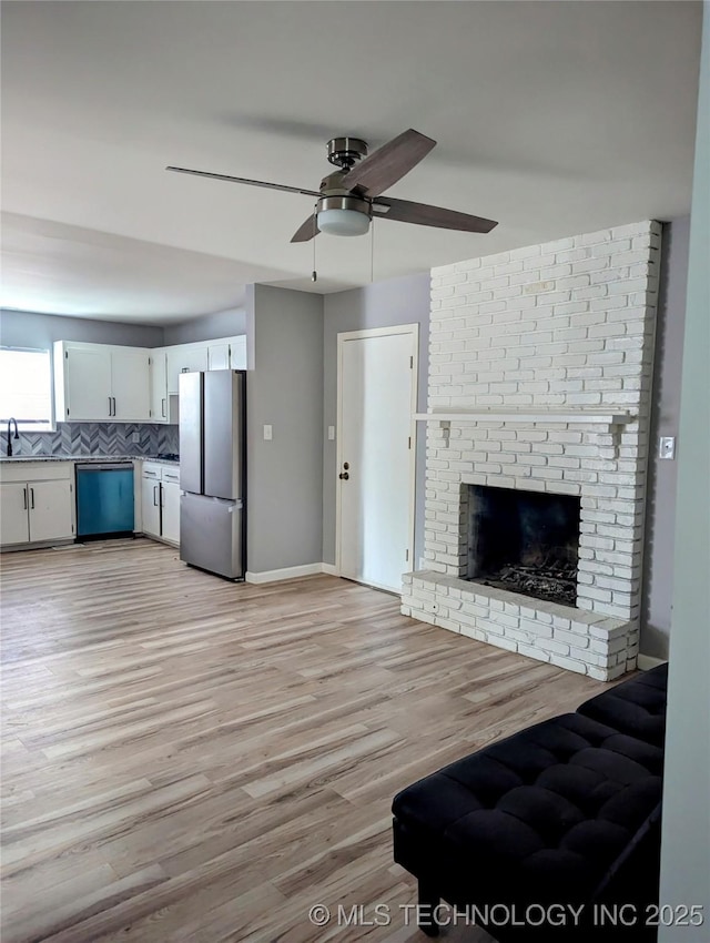 unfurnished living room featuring sink, a fireplace, light hardwood / wood-style floors, and ceiling fan