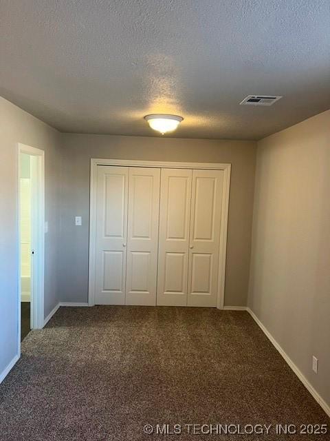 unfurnished bedroom featuring dark carpet, a closet, and a textured ceiling