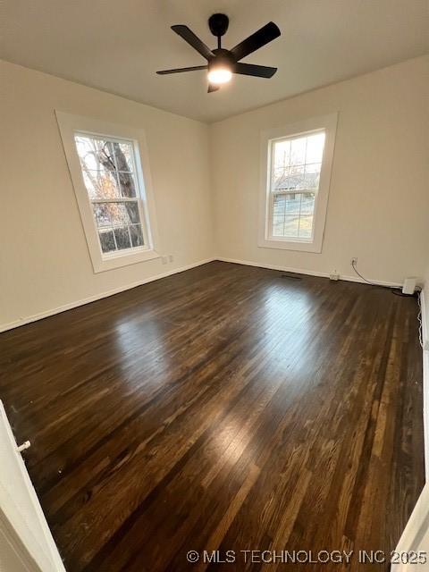 empty room featuring ceiling fan, a wealth of natural light, and dark hardwood / wood-style flooring