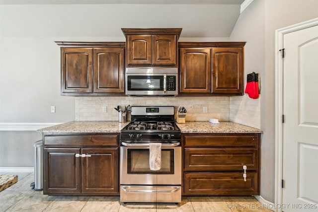 kitchen with dark brown cabinetry, stainless steel appliances, light stone countertops, and decorative backsplash