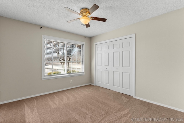 unfurnished bedroom with a textured ceiling, a closet, ceiling fan, and carpet flooring