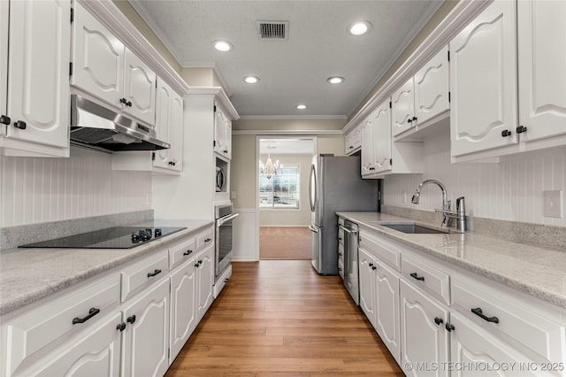 kitchen with appliances with stainless steel finishes, sink, white cabinets, ornamental molding, and light hardwood / wood-style flooring