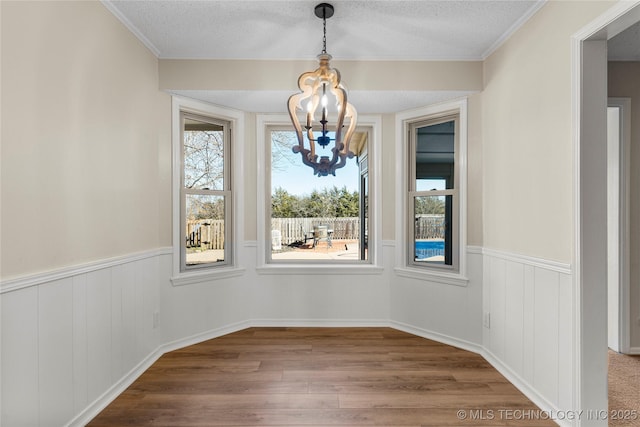 unfurnished dining area featuring an inviting chandelier, a textured ceiling, and hardwood / wood-style flooring