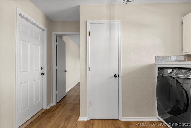 clothes washing area featuring washer / clothes dryer, light hardwood / wood-style floors, and cabinets