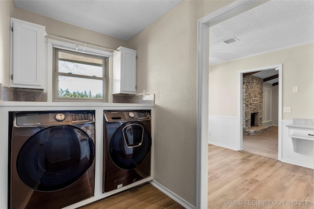 laundry area featuring a fireplace, cabinets, independent washer and dryer, a textured ceiling, and light hardwood / wood-style flooring