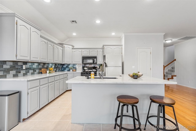 kitchen featuring an island with sink, sink, decorative backsplash, white refrigerator, and stove