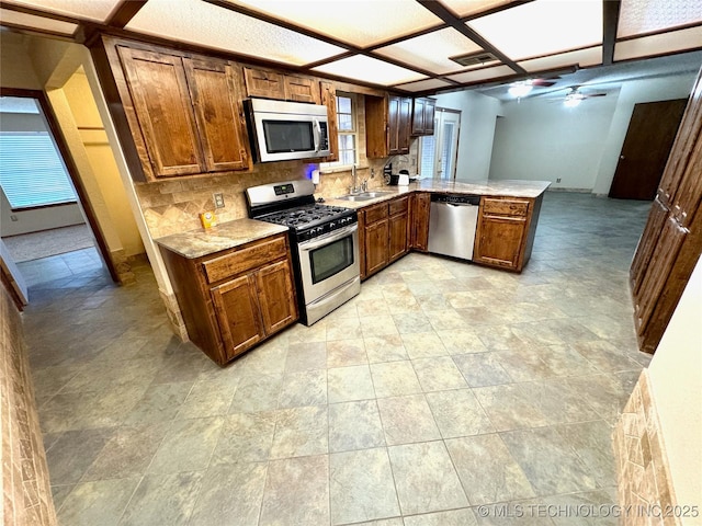 kitchen with sink, ceiling fan, stainless steel appliances, decorative backsplash, and kitchen peninsula