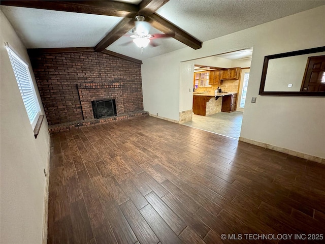 unfurnished living room featuring hardwood / wood-style floors, lofted ceiling with beams, ceiling fan, a brick fireplace, and a textured ceiling